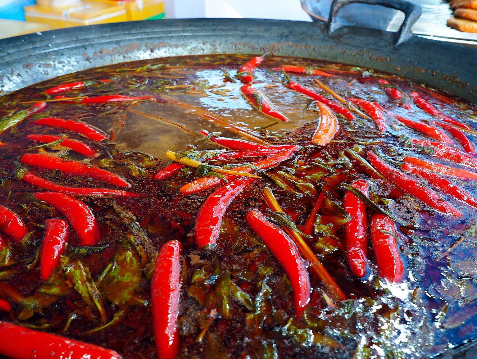 Chảo lớn với nhiều trái ớt đỏ nổi trên mặt nước sốt tại gian hàng ẩm thực