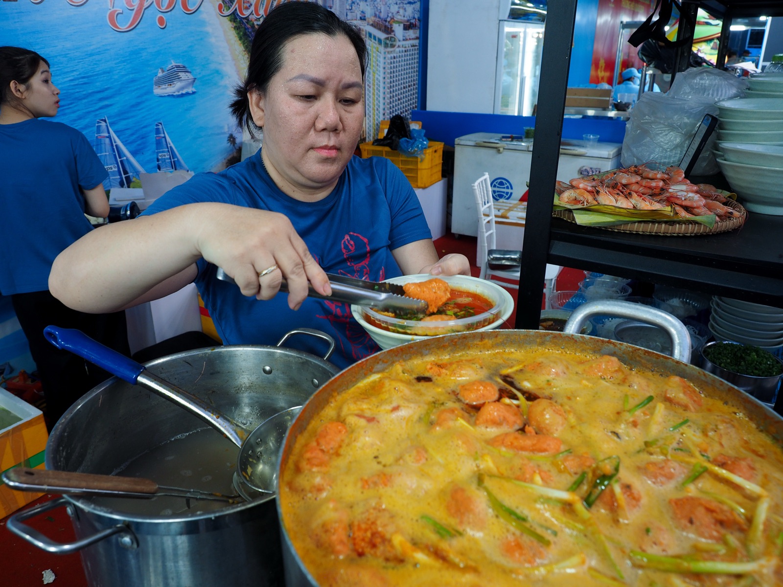 Người bán múc bánh canh từ nồi lớn sánh vàng, phía sau là khay hải sản luộc