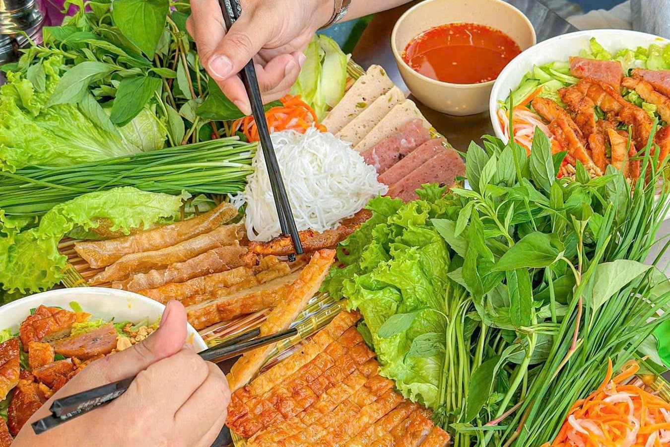 Một phần nem nướng bày cùng rau sống, bún, đồ chua và chén nước chấm