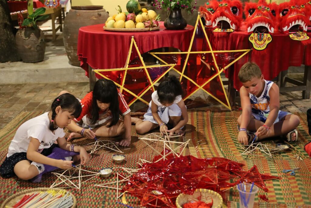 Trẻ em ngồi trên chiếu tự làm khung đèn ông sao bằng nan tre tại Làng nghề Nha Trang Xưa